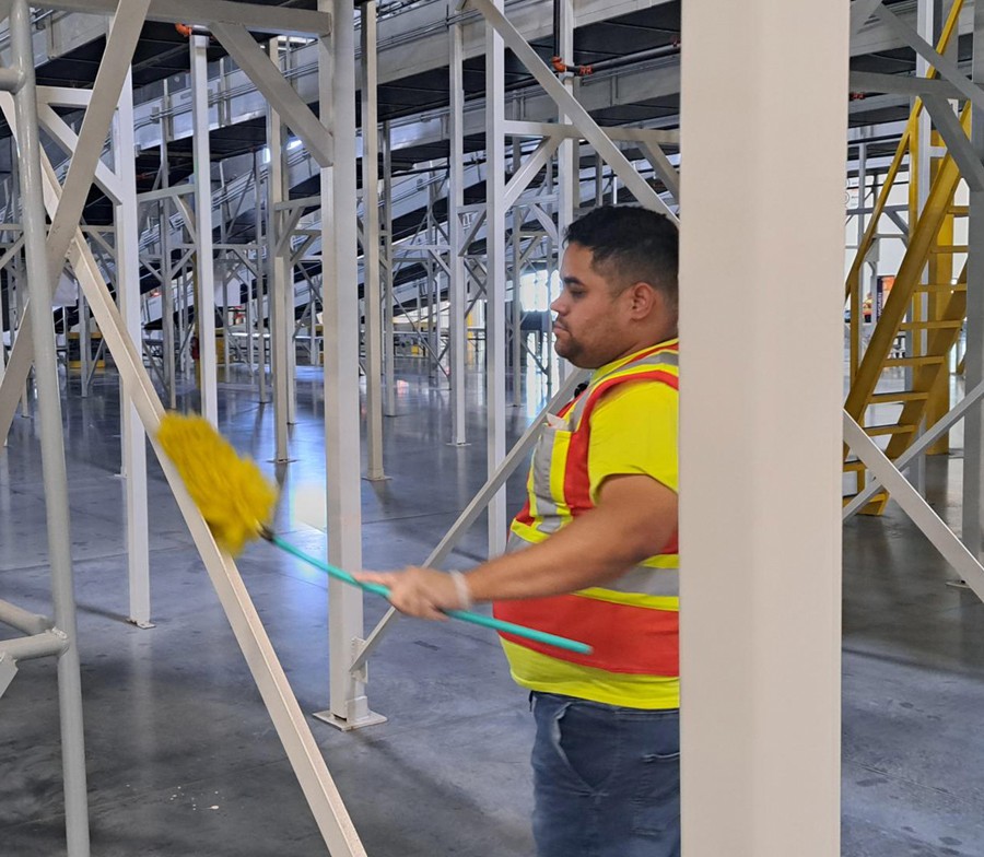 Commercial janitorial worker performing high-dusting services inside a warehouse facility as part of an industrial cleaning and facility maintenance program by All 1 Service.